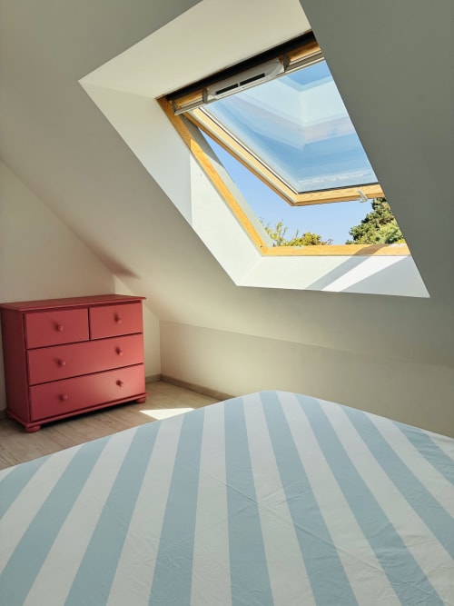 Chambre lumineuse sous les toits à Villa Métisse avec puits de lumière, literie rayée, commode rouge, parquet et vue sur Groix