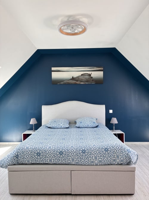 Chambre mansardée moderne aux murs bleus, lit blanc avec parure à motifs et photographie de jetée en bois au-dessus de la tête de lit à la Villa