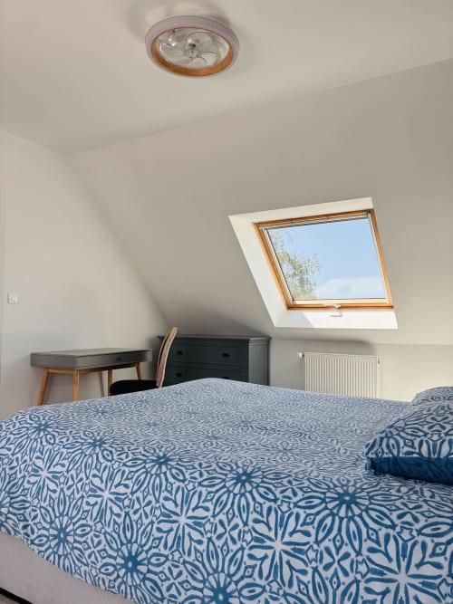 Chambre lumineuse sous les toits à la Villa Métisse à Groix avec lucarne, ventilateur de plafond en bois, literie bleue à motifs et style moderne