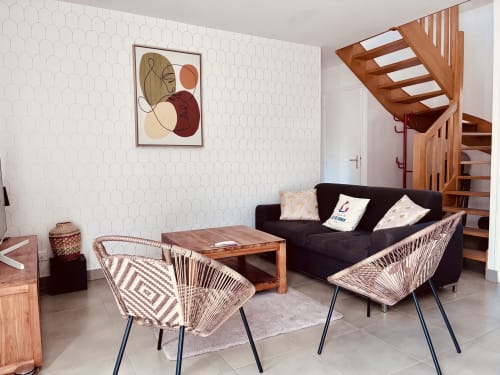Salon de villa contemporaine à Île et Villas Groix avec canapé noir, chaises tressées, table bois et escalier bois