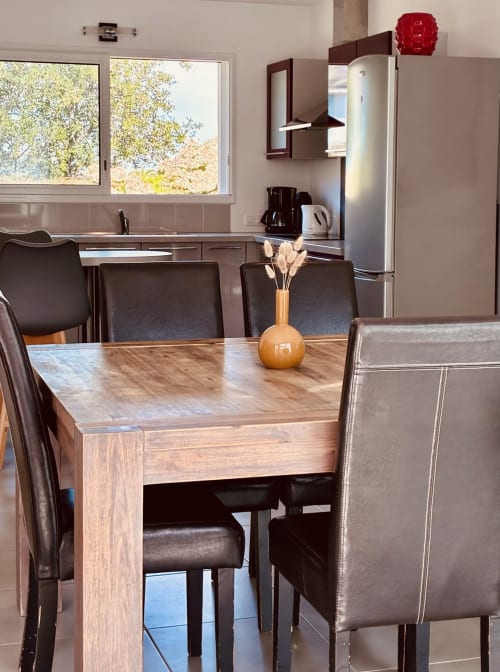 Salle à manger contemporaine avec table en bois, chaises en cuir marron et cuisine aux électroménagers inox à Villa Garance