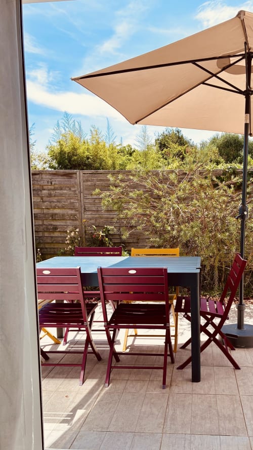 Terrasse ensoleillée avec chaises bordeaux, table bleue et parasol beige à Villa Garance à Groix