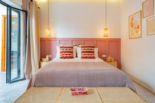Chambre moderne à M Résidences et Hôtels avec tête de lit corail, oreillers à motifs rouges, luminaires suspendus et accès à la terrasse