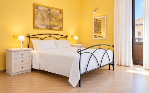 Bright yellow bedroom with wrought iron bed and white linens in Sicily In Home apartment, Catania