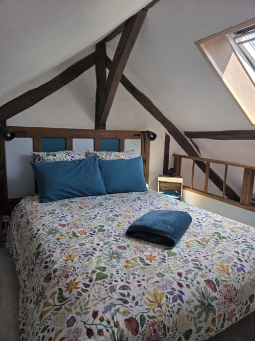 Chambre mansardée à La Maréchalerie, Lion en Sullias, avec poutres apparentes, linge de lit fleuri, oreillers bleus et vue sur le jardin