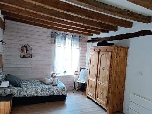 Chambre spacieuse avec poutres en bois, murs en lambris blanc, banquette fenêtre et armoire en pin à La Maréchalerie et le Nichoir