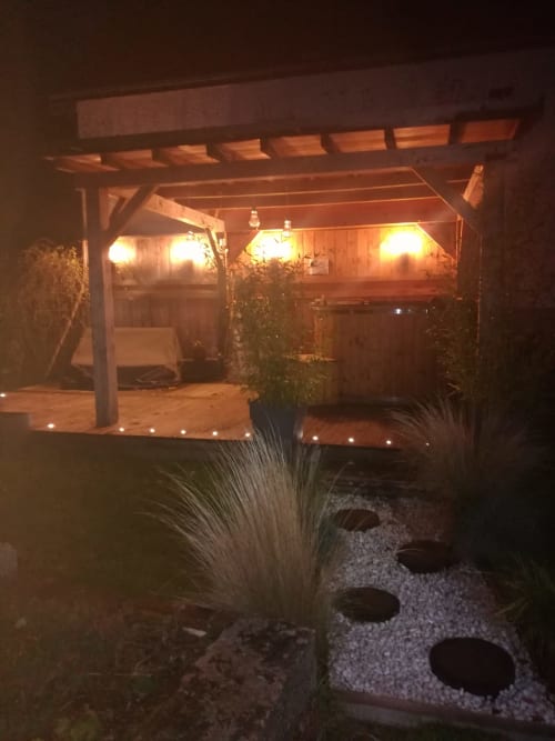 Pergola en bois illuminée sur la terrasse de nuit avec éclairage ambiant, plantes en pot et jardin de graviers à La Maréchalerie