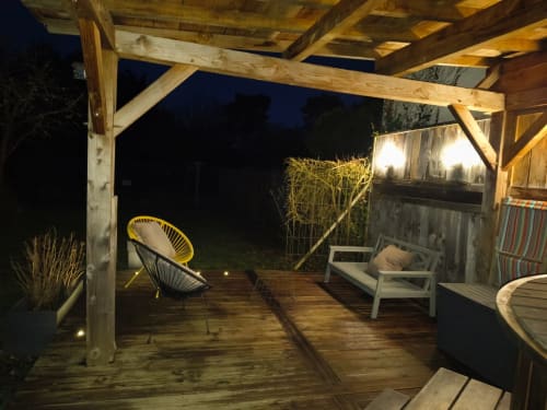 Terrasse en bois de nuit à La Maréchalerie avec chaise jaune, salon de détente, éclairage de jardin et vue sur le bain nordique
