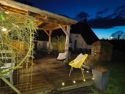 Vue du crépuscule à La Maréchalerie avec terrasse en bois, chaise jaune, pergola et allée illuminée à Lion en Sullias