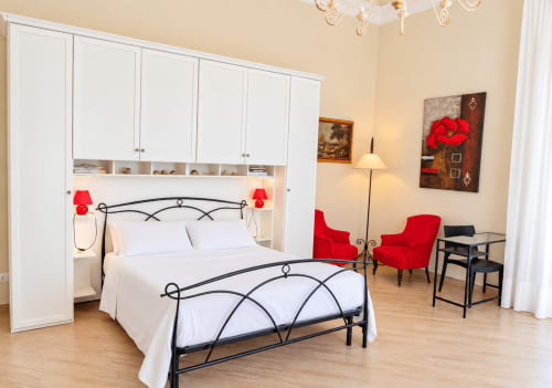 Spacious Red House apartment in Catania, Sicily with wrought iron bed, white cabinetry, red accent chairs, and modern