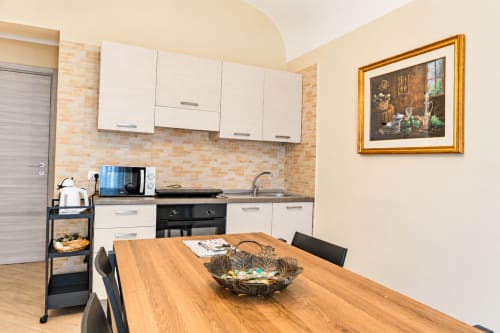 Modern kitchen in Red House apartment, Catania Sicily, with white cabinets, brick backsplash, and wooden dining table
