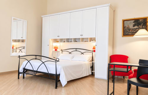 Modern bedroom in Catania apartment with black metal bed, white built-in wardrobes, red accents, and workspace at Sicily In
