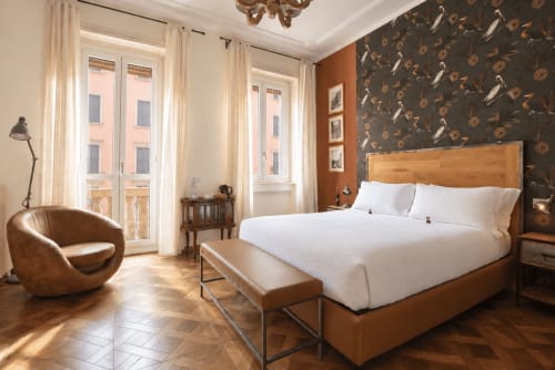Camera da letto di lusso a Porta Tosa Milano con letto in legno, vista sulla città, poltrona in pelle e carta da parati botanica scura