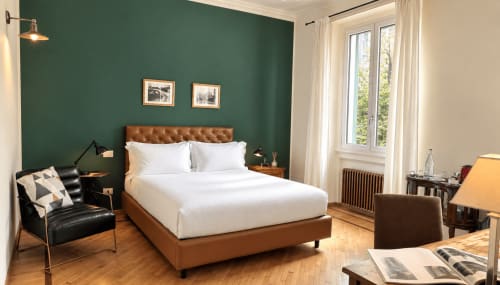 Elegante camera da letto a Porta Tosa Milano con pareti verdi, testata in pelle marrone, biancheria bianca e vista sulla città dalle finestre