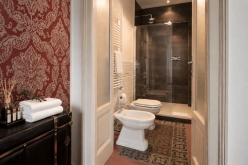 Bagno elegante a Porta Tosa Milano con carta da parati damascata, finiture bianche e doccia con piastrelle scure