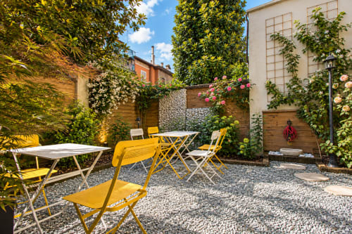 Soleggiato cortile della Porta Tosa B&B Milano con sedie gialle, tavoli da pranzo, piante rampicanti e fiori