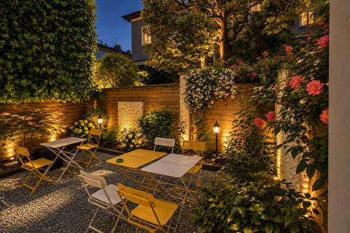 Cortile illuminato di Porta Tosa Milano con lettini, piante fiorite e muri ricoperti di edera al tramonto