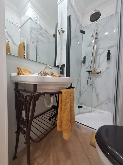 Luxury bathroom with marble walls, ornate sink vanity, walk-in shower, gold fixtures, and towel rack at Salamanca Luxury
