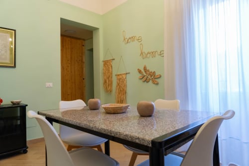 Moderna sala da pranzo nell'appartamento Green House a Catania, Sicilia, con tavolo in granito, sedie bianche e decorazioni su pareti verde menta