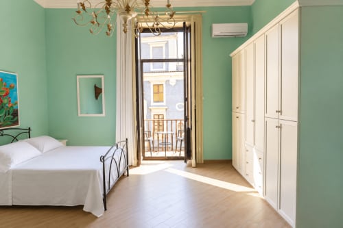 Luminosa camera da letto verde menta con letto in metallo bianco, armadio color panna, balcone con vista su Catania in Sicilia
