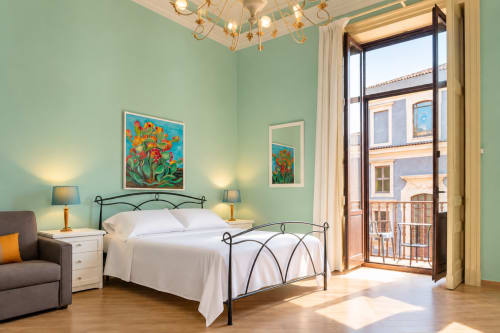 Bright mint green bedroom with wrought iron bed, artwork, and Catania city view balcony in Sicily apartment