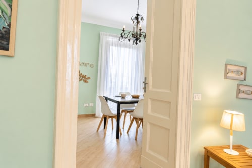 Zona pranzo dell'appartamento Green House con pareti menta, tavolo nero, sedie in legno, lampadario e vista sulla città di Catania, Sicilia