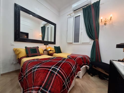 Luxury double bedroom at Salamanca Luxury Rooms Madrid with red tartan bedding, yellow pillows, and elegant furnishings