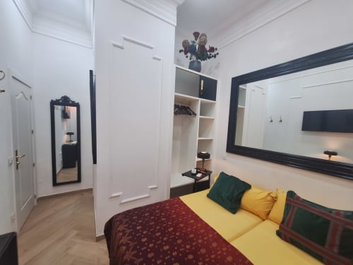 Modern double bedroom at Salamanca Luxury Rooms in Madrid with yellow bedding, white built-in wardrobes, black-framed mirror,