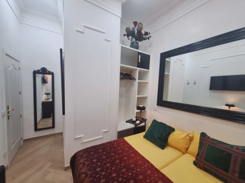 Modern double room at Salamanca Luxury Rooms Madrid with yellow bed, flat-screen TV, mirrored wardrobe, and white walls