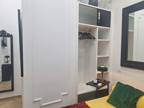 Modern bedroom at Salamanca Luxury Rooms Madrid with white built-in wardrobe, mirror, and yellow bed with green pillow