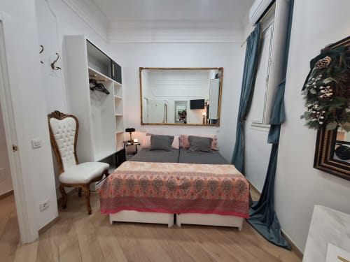 Elegant double bedroom at Salamanca Luxury Rooms in Madrid with ornate mirror, decorative chair, and blue curtains
