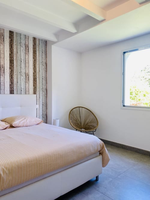 Chambre moderne de la Villa Métisse à Groix avec mur en bois, lit blanc, linge rayé, fauteuil en rotin et fenêtre