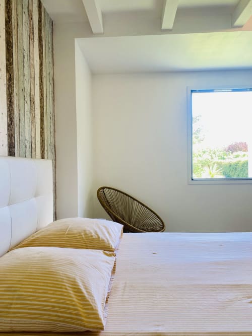 Chambre moderne avec literie à rayures jaunes, tête de lit en bois, fauteuil tissé et vue sur le jardin à Villa Métisse, Groix