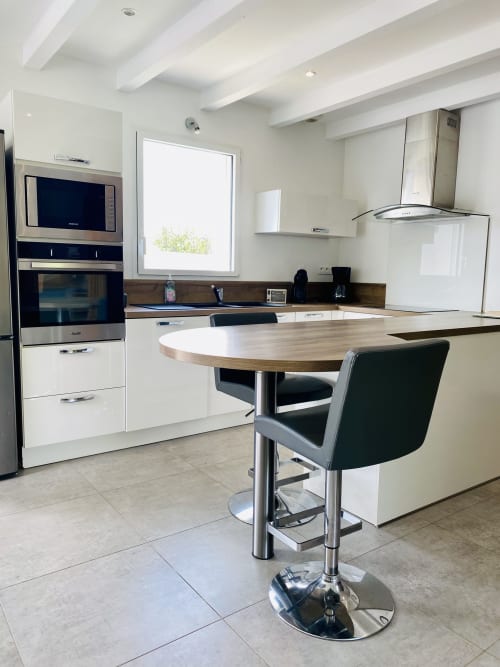 Cuisine moderne avec armoires blanches, électroménagers en acier inoxydable et table de salle à manger ronde avec chaises noires à la Villa Métisse