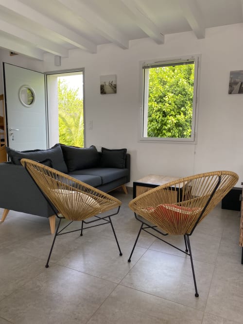 Salon moderne avec fauteuils tressés, canapé noir et vue luxuriante sur la verdure à Villa Métisse à Groix
