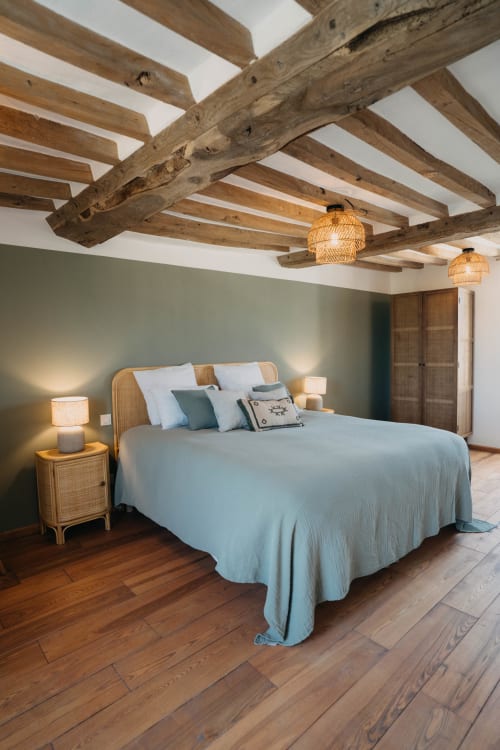 Suite chambre moderne au Clos d'Omaha avec poutres apparentes, literie bleu clair, luminaires suspendus en rotin et vert sauge