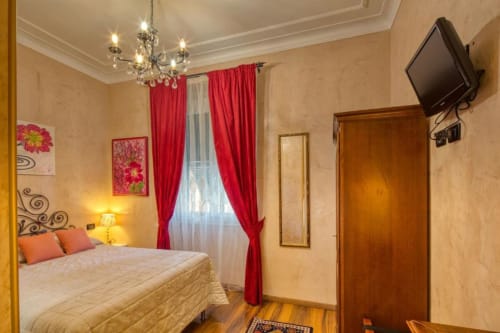 Camera elegante di Villa Moderna Genova con letto matrimoniale, tende rosse, lampadario in cristallo e TV a schermo piatto