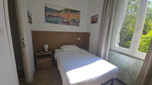 Camera singola standard dell'Hotel Villa Moderna a Genova con letto, testiera in legno, comodino e finestre con vista sul giardino