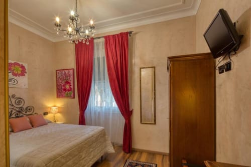 Elegante camera doppia all'Hotel Villa Moderna di Genova con tende rosse, lampadario, TV a schermo piatto e pavimenti in legno.
