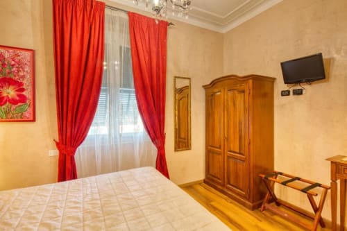 Camera matrimoniale standard dell'Hotel Villa Moderna a Genova con tende rosse, armadio in legno, TV a schermo piatto e pavimenti in parquet