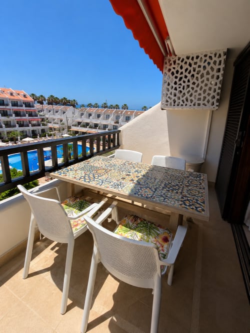 Sunny balcony at Manage Home Tenerife with dining table, white chairs, pool view, and resort buildings in Playa de Las