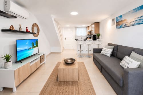 Modern living room in Duplex Michelle apartment at Playa de Las Americas with gray sofa, wooden TV stand, kitchen bar, and