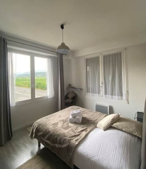 Chambre lumineuse à La Maison de Barlest avec vue sur la campagne, linge de lit beige, suspension et paysage verdoyant.