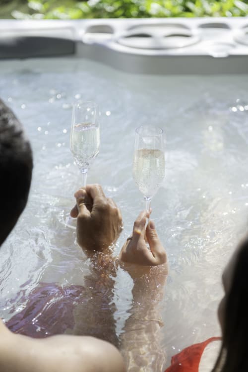 Deux personnes dans une piscine tenant des flûtes de champagne au Le chant des pins Lodges & Spas, Saint-Marc-Jaumegarde