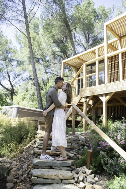 Couple s'embrassant sur les marches de pierre du Chant des Pins Lodges & Spas, Saint-Marc-Jaumegarde, avec lodge en bois moderne et forêt