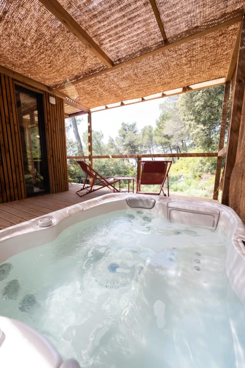 Bain à remous extérieur sur terrasse en bois à Le chant des pins Lodges & Spas, avec vue sur la forêt et auvent tissé