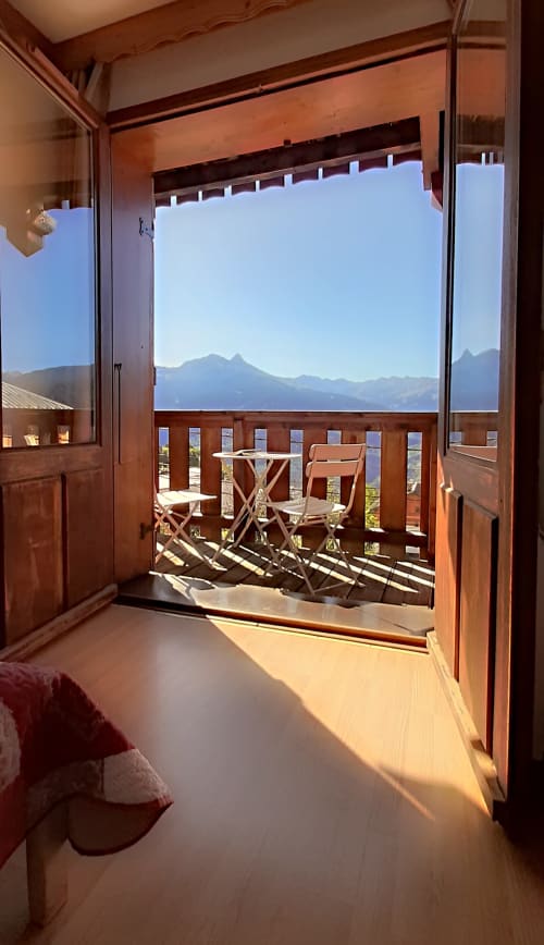 Vue panoramique des Alpes depuis le balcon de la chambre du Chalet De La Yodine, mobilier en bois et terrasse ensoleillée