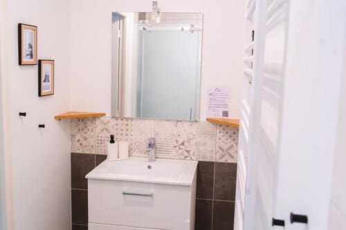 Modern bathroom in Nairobi Apartment at Résidence des Sables, Mably, featuring white sink, wood shelves, patterned tile