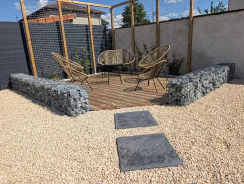 Private courtyard patio at Résidence des Sables with wicker chairs, wooden deck, gravel landscaping, and mesh privacy screens