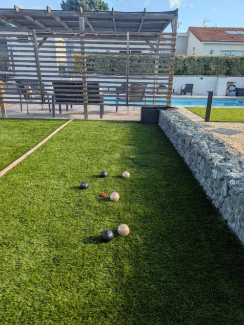 Bocce ball game in progress on artificial turf lawn at Résidence des Sables, Mably, with poolside pergola and courtyard view.